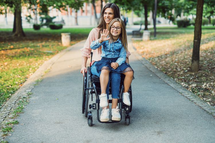 Mum in a manual wheelchair with a little girl on her laop.
