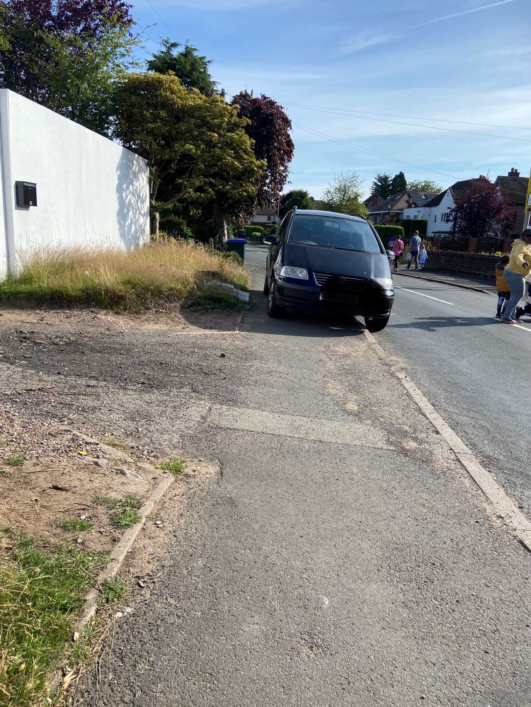 A car completely blocks the pavement for pedestrians.