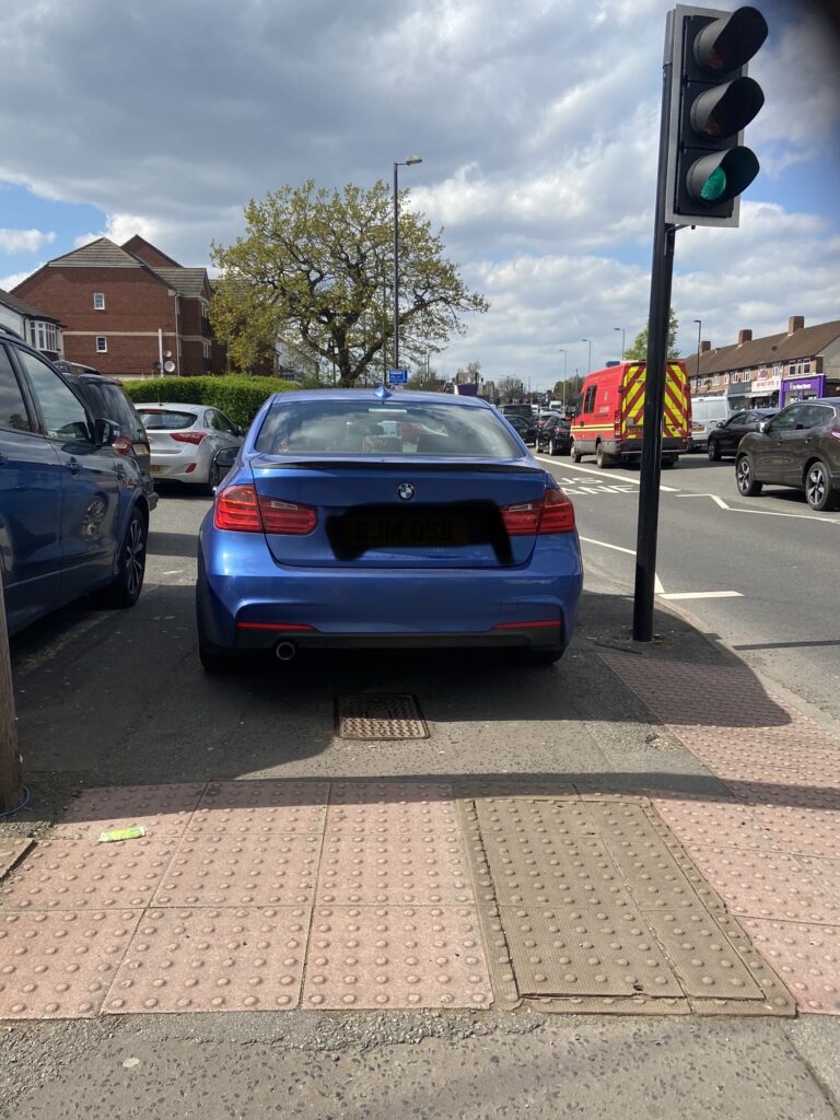 A car blocks the pavement beside a pedestrian crossing.