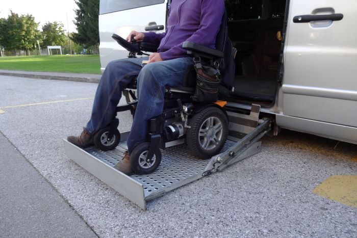 A man in an electric wheelchair is on a lift going into a taxi