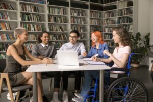 A wheelchair user is sat around a table with a small group of young people