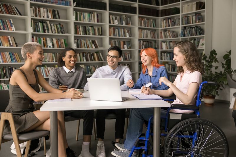 A wheelchair user is sat around a table with a small group of young people