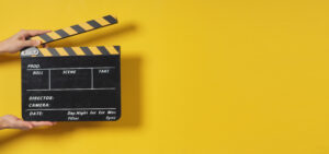 Yellow background with a clapper to the left with a hand holding it